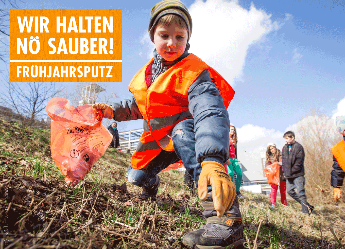 Auf dem Bild ist ein junger Bub mit einer orangen Warnweste, orange Handschuhe sowie einen orangen Mllsack zu erkennen. Das Kind greift am Boden. Im Hintergrund sind weitere Kinder zu erkennen.